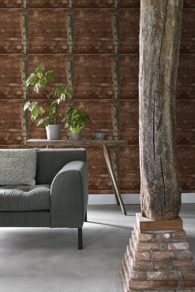 Wohnzimmer mit grauer Couch, Holztisch mit Pflanzen, dekorativer Holzsäule und Wandtapete in Fliesenoptik