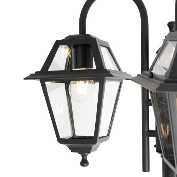 Schwarze Außenleuchte in klassischer Laternenform aus Metall mit Glaseinsätzen und brennendem Leuchtmittel.
