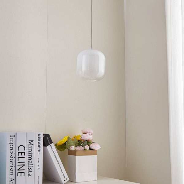 Moderne Pendelleuchte mit Glasschirm in einem hellen, minimalistischen Raum über einem Tisch mit Dekoration.