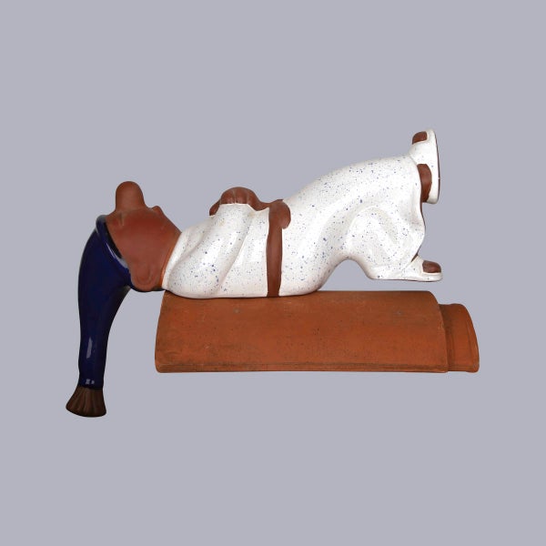Firstfigur schlafender Mann auf Dachziegel aus Keramik mit blauer Schlafmütze und weißem Schlafanzug.