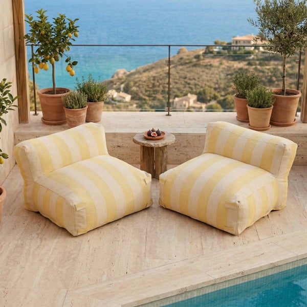 Zwei gestreifte Outdoor-Bodenkissen auf einer Steinterrasse mit Pool und Blick auf das Meer.