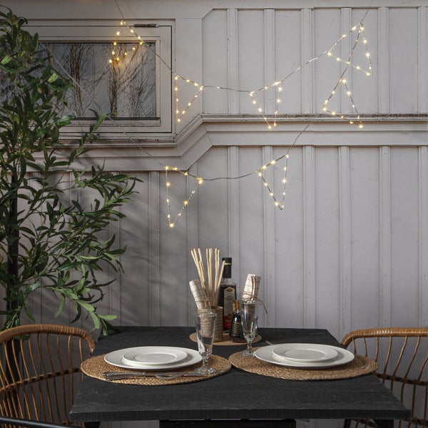 Festlich gedeckter Esstisch mit Dreieck-Lichterkette und Pflanze