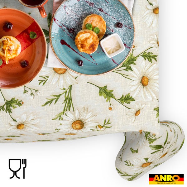 Abwaschbare Tischdecke mit großem Gänseblümchen-Muster und grünen Blättern. Lebensmittelecht Symbol und ANRO Deutsche Manufaktur Logo.