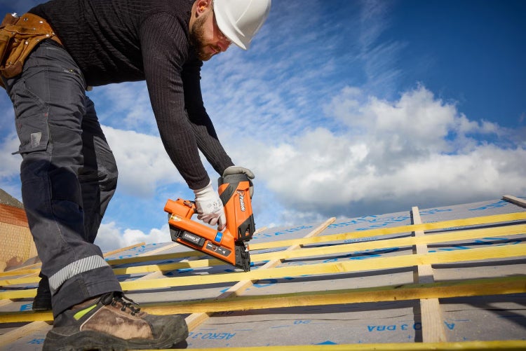 Handwerker mit Paslode Druckluftnagler bei der Arbeit auf einem Dachstuhl mit Unterspannbahn und Lattung.