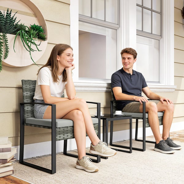 Ein Paar auf einem modernen Garten-Set aus zwei grauen Polyrattan-Stühlen mit Metallgestell und Beistelltisch auf einer hellen Terrasse.