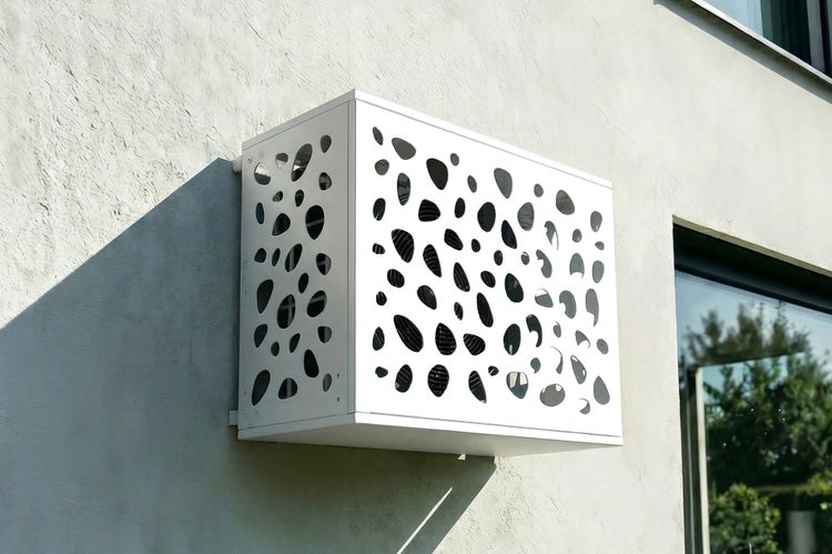 Klimaanlagenverkleidung mit dekorativen Aussparungen an einer Hauswand montiert