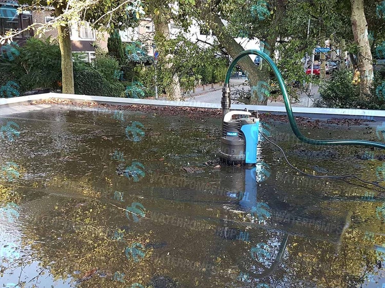 Eine Tauchpumpe steht in einer Wasserpfütze auf einem Dach und pumpt Wasser ab.