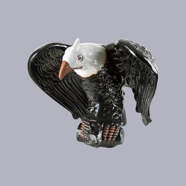 Dekorative Adlerfigur aus Keramik in Schwarz und Weiß mit ausgebreiteten Flügeln auf einem Ast.