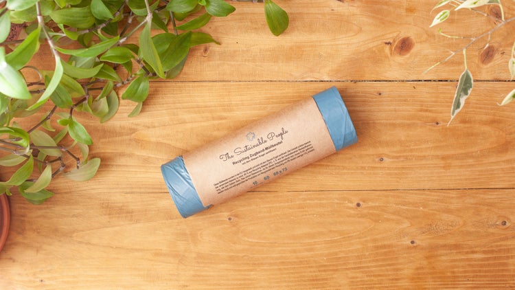 Eine Rolle The Sustainable People Recycling Zugband Müllbeutel aus hundert Prozent Altplastik auf einem Holztisch mit Pflanzen dekoriert.