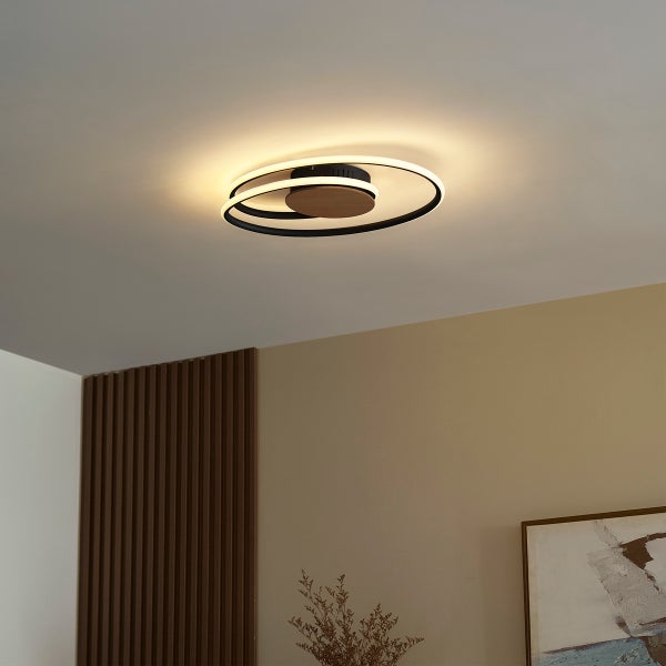 Moderne LED Deckenleuchte in Ringform mit Holzelementen montiert an einer Wohnzimmerdecke.