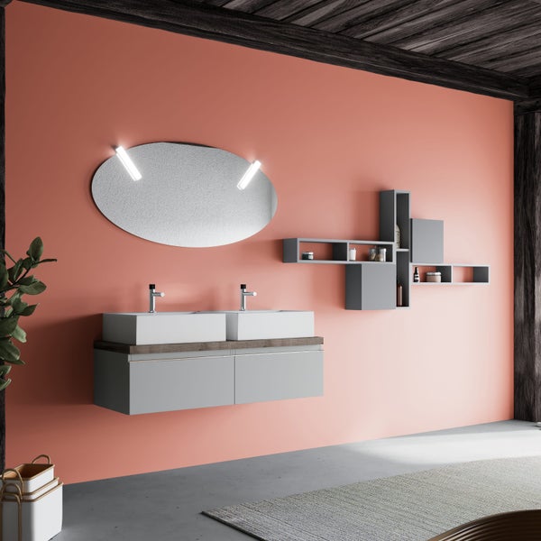 Modernes Badezimmer mit grauem Doppelwaschtisch, ovalem LED-Spiegel und grauen Wandregalen vor einer lachsfarbenen Wand.
