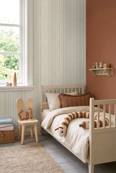 Ein Kinderzimmer mit gestreifter Tapete, hellem Holzbett, passendem Kinderstuhl, weicher Bettwäsche, Kuscheltier und einem kleinen Wandregal.