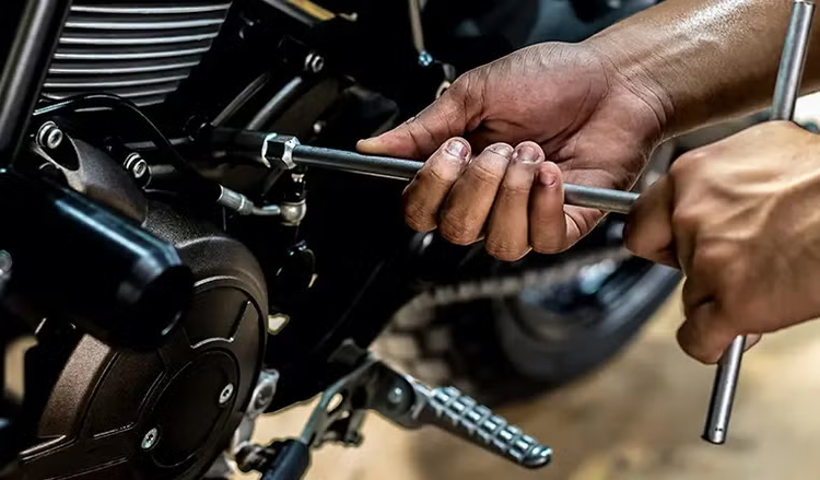 Eine Hand benutzt einen T-Griff-Steckschlüssel, um eine Schraube am Motorblock eines Motorrads festzuziehen.