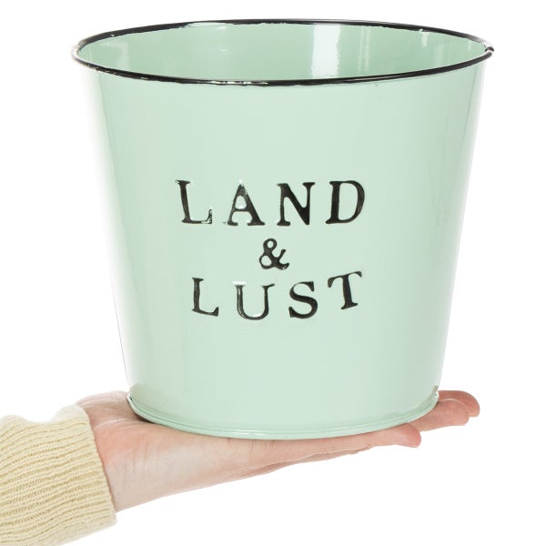 Mintgrüner Übertopf aus Metall mit schwarzem Rand und Aufschrift Land und Lust, in der Hand zur Größenveranschaulichung