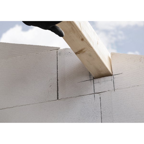 Ein Holzbalken wird in die Aussparung einer Wand aus Porenbetonsteinen eingeführt.