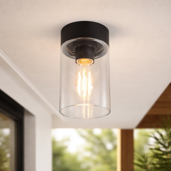 Zylindrische Außen-Deckenleuchte aus Glas und schwarzem Metall mit leuchtendem Filament-Leuchtmittel montiert an einer Decke.