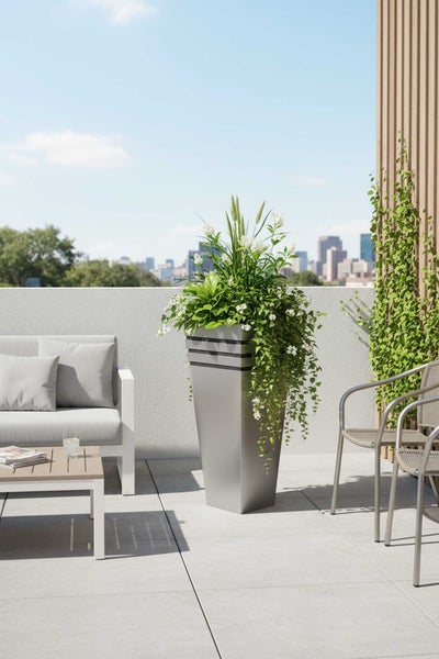 Moderner, hoher grauer Pflanzkübel auf einer Dachterrasse mit Bepflanzung, Gartenmöbeln und Blick auf die Skyline der Stadt.