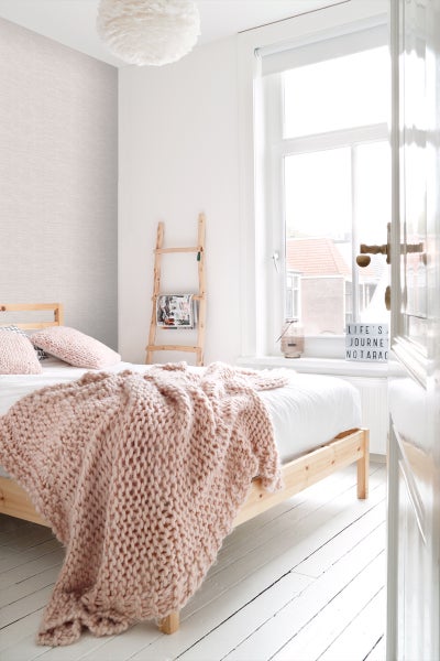 Helles Schlafzimmer mit Bett, Strickdecke und Holzleiter als Dekoration