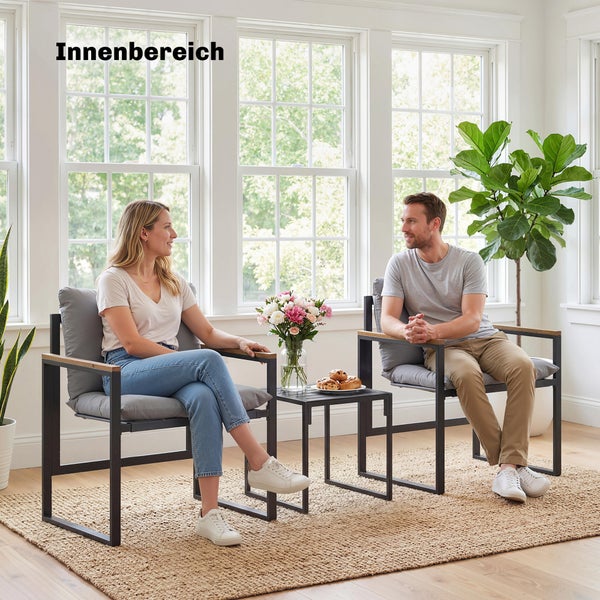 Moderne Indoor-Sitzgruppe mit zwei Sesseln aus schwarzem Metall, grauen Polstern und Beistelltisch auf einem Jute-Teppich in hellem Raum.