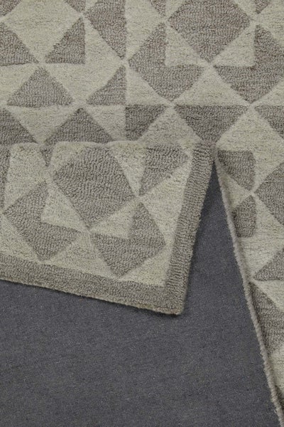 Nahaufnahme eines Teppichs mit geometrischem Dreiecksmuster und umgeschlagener Ecke, die die dunkle Rückseite zeigt.
