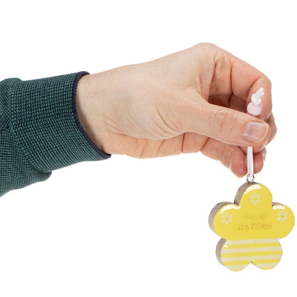 Hand hält Osteranhänger in Blumenform mit der Aufschrift Frohe Ostern