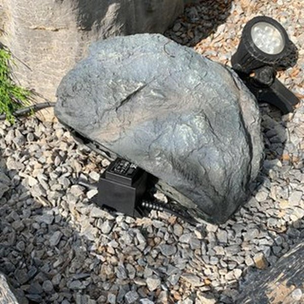 Künstlicher Stein zur Abdeckung von Teichtechnik und Gartenbeleuchtung auf Kies.