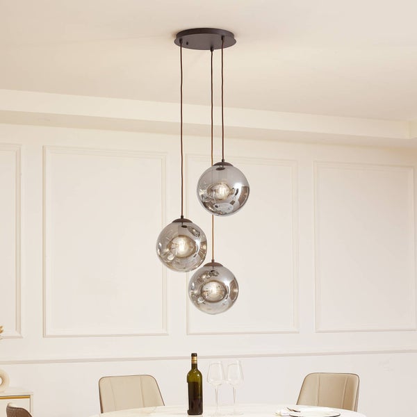 Moderne Pendelleuchte mit drei kugelförmigen Rauchglasschirmen, die in unterschiedlichen Höhen in einem hellen Esszimmer hängen.