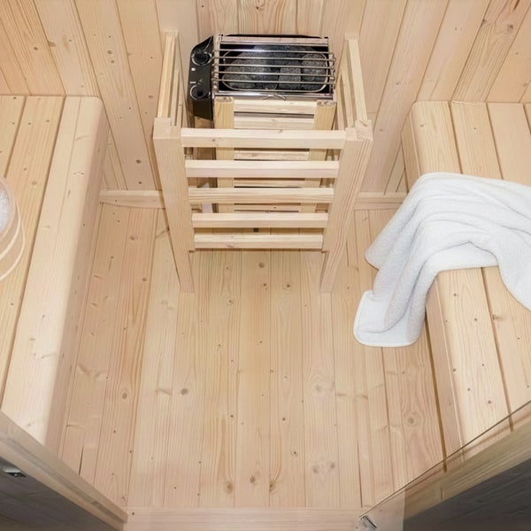 Innenansicht einer Sauna mit Holzwänden und Saunabänken, in der Mitte ein Saunaofen mit Schutzgitter und Steinen, ein Handtuch liegt auf der Bank.