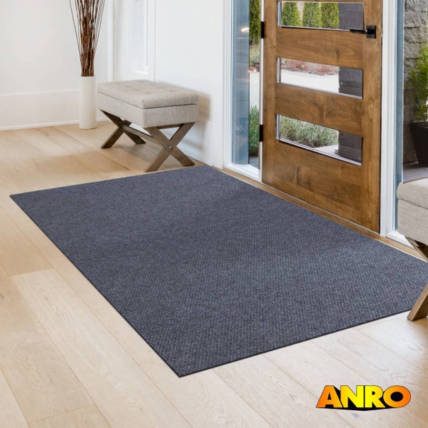 Rechteckige Schmutzfangmatte im hellen Eingangsbereich vor einer Holztür auf hellem Holzboden. ANRO Logo.