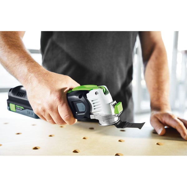 Eine Person hält ein Festool 18 Volt Akku-Oszillierer Multitool mit Sägeblatt über einer Werkbank aus Holz.