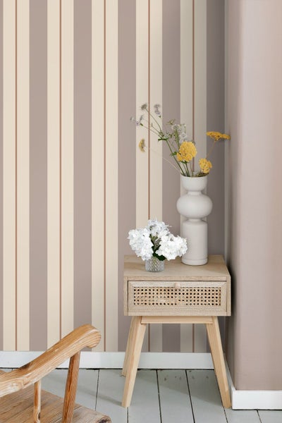 Moderne Raumszene mit gestreifter Tapete in Beige und Braun. Ein hölzerner Beistelltisch mit Rattan-Schublade und Blumen steht vor der Wand.