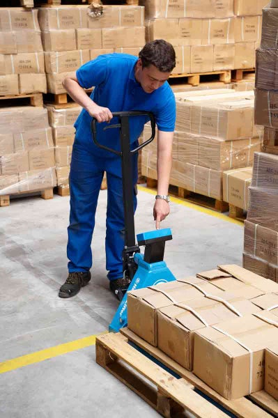 Mitarbeiter bedient einen Hubwagen mit Waage in einem Lager, um eine Palette mit Kartons zu wiegen.