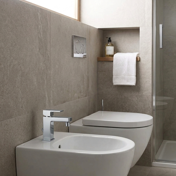 Modernes Badezimmer mit wandhängendem Bidet, WC, verchromter Armatur und großflächigen Fliesen in Steinoptik.
