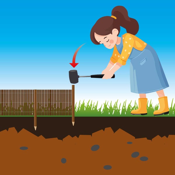 Eine Person schlägt mit einem Gummihammer einen Holzpfosten für einen Gartenzaun in den Boden.