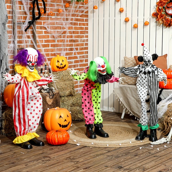 Drei gruselige Halloween Clown Figuren als Dekoration vor einer Ziegelwand mit Strohballen, Kürbissen, Spinnenweben und Lichterkette.