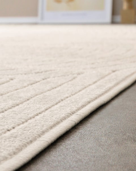 Detailaufnahme eines hellen Teppichs mit strukturiertem Linienmuster und geketteltem Rand.