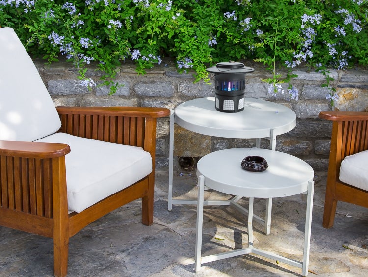 Szene mit zwei Holzstühlen mit Polsterung, einem zweistufigen Beistelltisch mit einer Insektenfalle und einem Aschenbecher