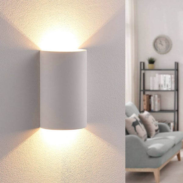 Moderne zylindrische Wandleuchte mit Up-and-Down-Lichteffekt an einer verputzten Wand in einem Wohnzimmer.
