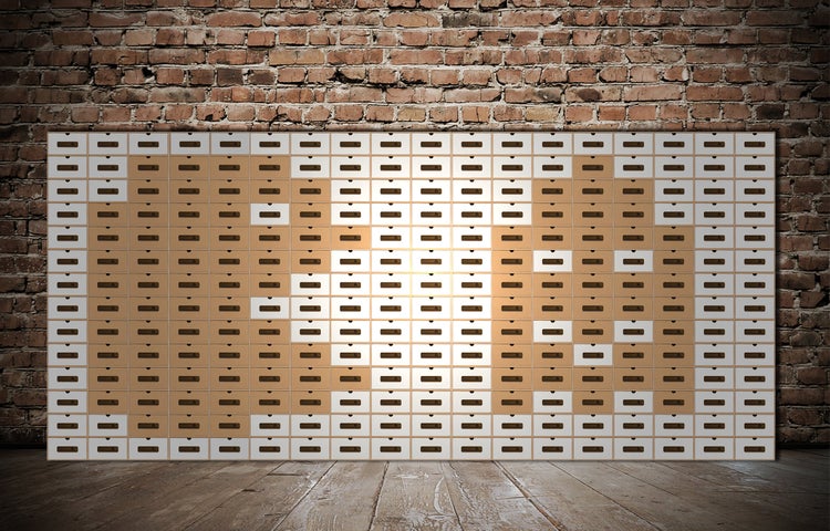 Wand mit vielen gestapelten Karton-Archivboxen vor einer rustikalen Backsteinmauer und Holzboden.