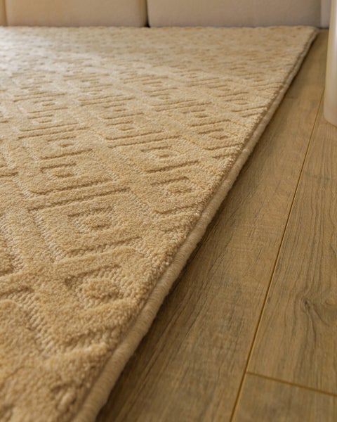 Nahaufnahme eines strukturierten Teppichs mit geometrischem Muster auf einem Holzboden.