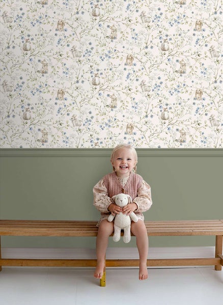 Tapete mit Hasen und Blumenmuster in einem Kinderzimmer mit einer Holzbank und einem sitzenden Kind