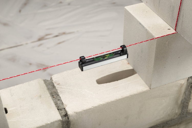 Wasserwaage mit Richtschnur vor einer Backsteinmauer
