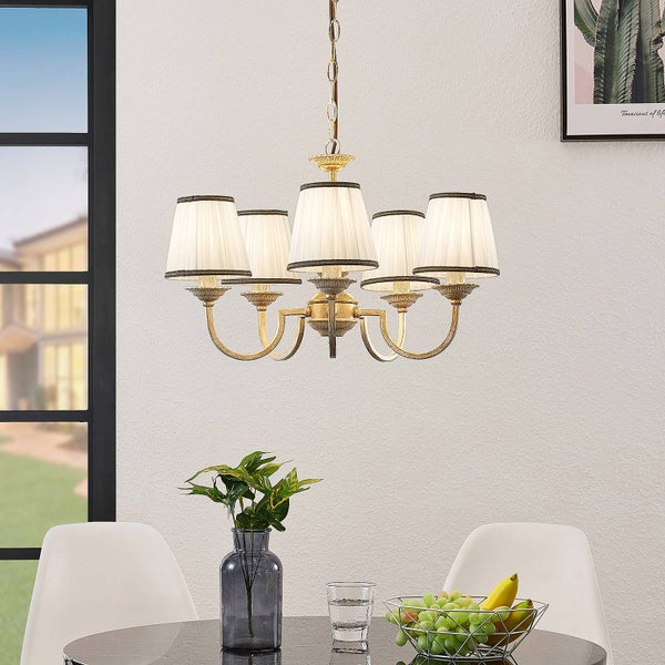 Fünfflammiger Kronleuchter mit weißen Stoffschirmen und messingfarbenem Metallgestell über einem Esstisch in einem hellen Raum.