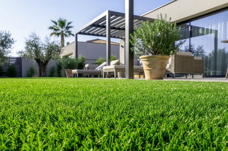 Gepflegter Rasen vor einer modernen Terrasse mit Pergola und Sitzmöbeln bei strahlendem Sonnenschein.