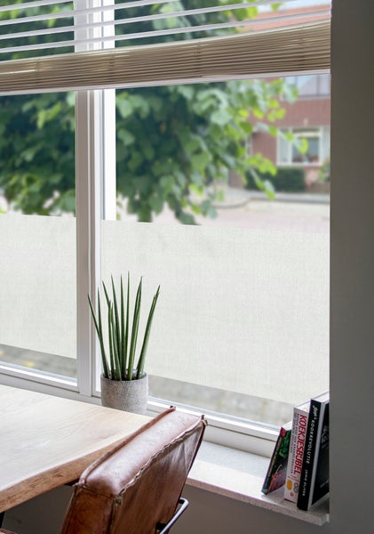 Statisch haftende Sichtschutzfolie in Leinenoptik an einem Fenster mit Zimmerpflanze und Büchern auf der Fensterbank.