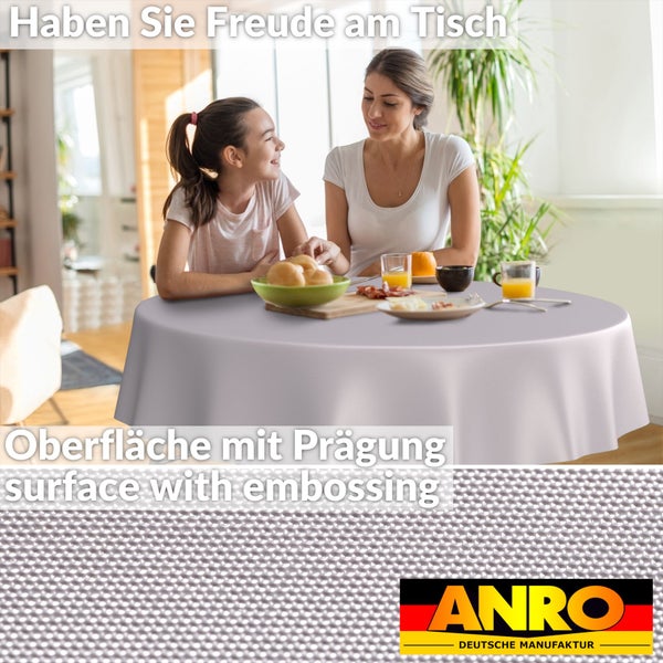 Runde geprägte Tischdecke im hellen Esszimmer mit Frau und Kind am Tisch. Detailansicht der geprägten Oberfläche. ANRO Logo.