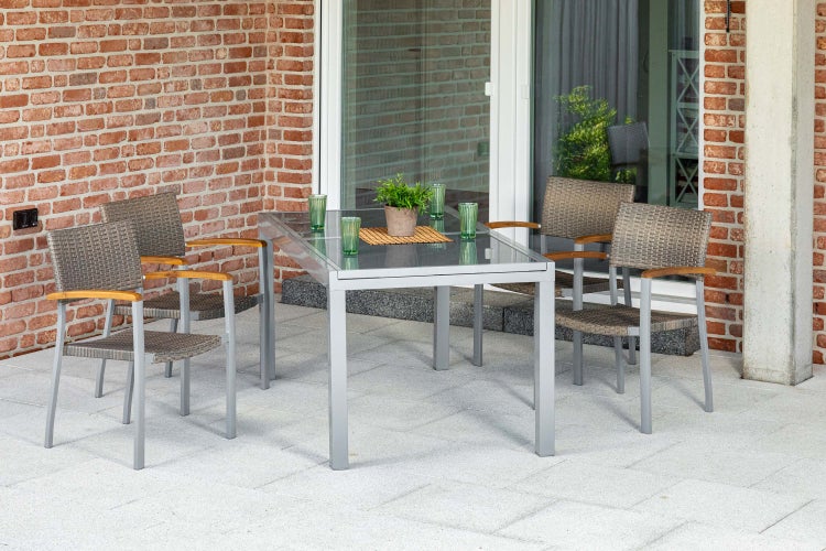 Moderne Gartenmöbel-Sitzgruppe mit Glastisch und vier Geflechtstühlen mit Holzarmlehnen auf einer gepflasterten Terrasse.