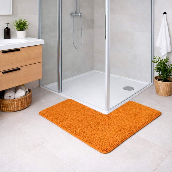 Orangefarbene Eck-Badematte vor einer Duschkabine aus Glas in einem hellen Badezimmer mit Holzmöbeln und Fliesen.