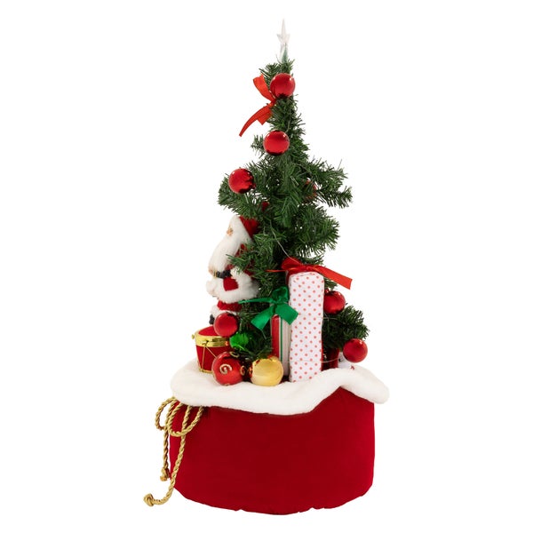 Künstlicher Weihnachtsbaum im Geschenkesack dekoriert mit Weihnachtskugeln und einer Weihnachtsmannfigur
