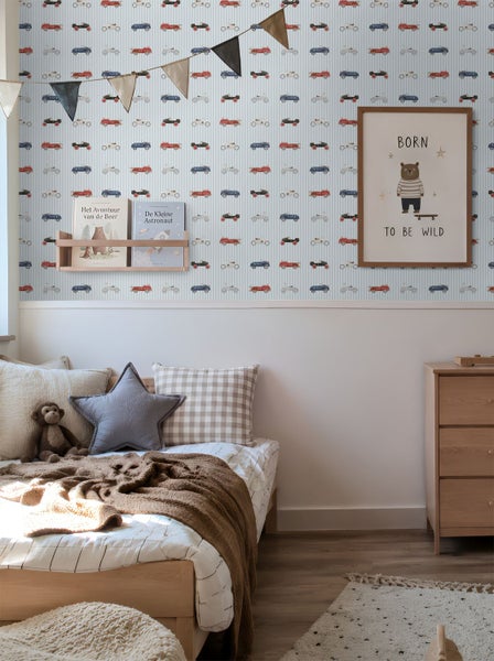Vliestapete im Kinderzimmer mit Oldtimer-Motiv auf gestreiftem Hintergrund über einem Bett und einer Kommode aus Holz.